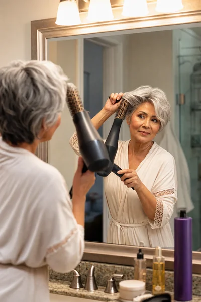 Short Gray Haircuts for Women Over 50: The Complete Guide 6 Woman styling short gray hair at bathroom mirror — daily hair care routine for mature women