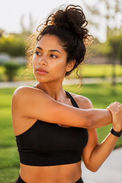 Woman in workout clothes wearing natural messy bun while stretching outdoors